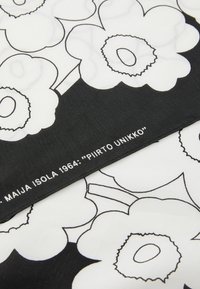 Tessuto floreale con grandi fiori bianchi contornati di nero su sfondo bianco, con un bordo inferiore nero che presenta dettagli testuali.