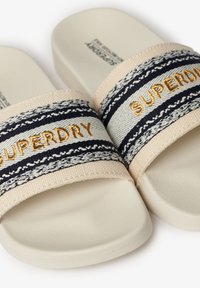 Beige slip-on sandalen met donkerblauwe gestreepte textielen banden met gouden "SUPERDRY" borduring. Gecoate rubberen zool voor grip.