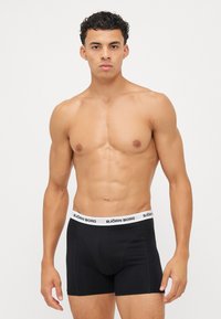 Boxeri negri cu un brâu elastic alb ce prezintă brandingul "BJÖRN BORG". Materialul este moale și elastic, aderând strâns de corp.