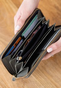 Two hands holding an open zippered wallet showing multiple card slots and compartments with cards and cash inside.