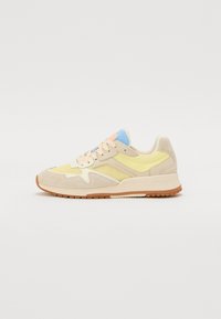 Sneaker beige et jaune avec une tige en daim et en maille, présentant des accents bleu pastel, des lacets rose clair et une semelle en caoutchouc texturée.