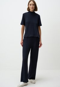 Marineblauw gebreid topje met een korte hoge hals, gecombineerd met bijpassende wijde broek. Gestructureerde stof; zachte afwerking; witte sneakers maken de outfit compleet.