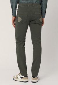 Chinos verde oliva con corte slim, que presentan bolsillos traseros inclinados con parches de tejido en contraste y una textura suave y mate.