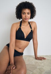 Sorte bikini-set med halterneck-topp med gullaccent og lavt liv. Glatt tekstur, enkelt design. Lett stoff.