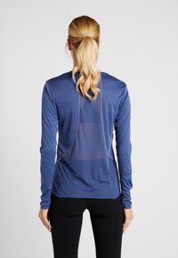 Camiseta deportiva de manga larga en tejido azul intenso con panel trasero de malla y costuras en contraste. Textura suave y diseño ceñido.