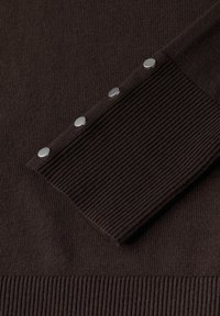 Tessuto a maglia marrone con texture a coste; presenta cinque bottoni metallici argento lungo la manica per la chiusura.