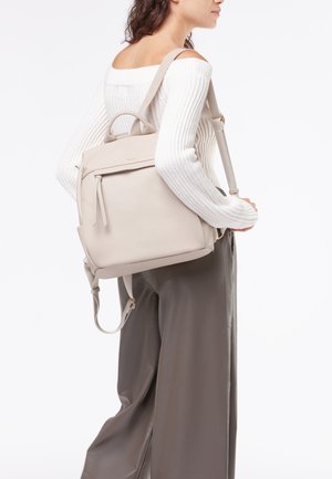 Zaino in pelle beige con un design strutturato, dotato di spallacci regolabili, una tasca anteriore con zip e manico superiore per il trasporto. Texture liscia.