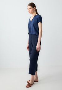 T-shirt bleu marine à col en V associé à un pantalon texturé, longueur genou. Le mannequin porte des sandales à brides brunes. Design simple et élégant.