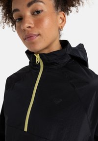 Black nylon jacket with a high collar and adjustable hood. Features a contrasting yellow zipper and subtle textured pattern.