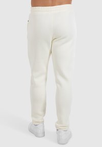 Weiße Sweatpants aus weichem Material mit einem elastischen Taillenbund und Taschen an den Seiten. Kombiniert mit weißen Turnschuhen.