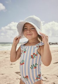 Badeanzug mit blauen und weißen Streifen, rüschendetail an den Schultern, verziert mit rotem Kirsch-Stickerei. Ein breitkrempiger, gestreifter Hut rundet den Look ab.