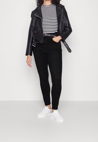 Chaqueta de cuero negro de motociclista sobre una camisa a rayas blancas y negras, combinada con pantalones ajustados negros y zapatillas blancas.