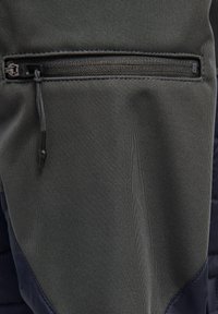 Close-up van donker stof met een horizontale ritszak en trekkoord op een kledingstuk.