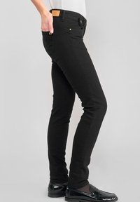 Jeans en denim noir avec une coupe ajustée, dotés d'une taille mi-haute, de passants de ceinture et d'une discrète étiquette logo au dos. Texture lisse.