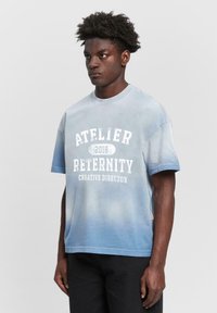 Light blue short-sleeve T-shirt with a gradient design, featuring white text: "ATELIER RETERNITY 2018 CREATIVE DIRECTOR." Casual fit.