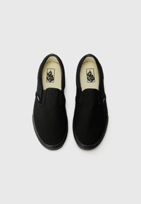 Chaussures slip-on noires en toile avec un bout rond et des semelles en caoutchouc noires. Présentent une étiquette de logo sur le côté et une semelle intérieure beige. Texture lisse.