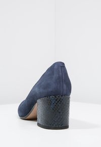 Chaussure à talon bloc en cuir suédé bleu marine avec un talon noir texturé et un bout arrondi, présentée sur un fond blanc dans un coin.