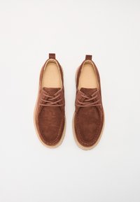 Chaussures en daim marron avec un bout rond, des coutures contrastantes et un design à lacets. Équipées d'une languette au talon et d'une doublure intérieure lisse.