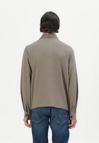 Long-sleeve, olive polo shirt with a relaxed fit, featuring a buttoned cuff and a smooth texture, paired with blue jeans.