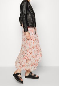 Veste de motard en cuir noir, jupe maxi rose à motifs floraux, et sandales noires avec des accents cloutés. La tenue présente un design superposé et fluide.