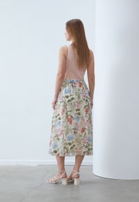 Floral midi skirt in light fabric with multicolored plant patterns, paired with a nude tank top and beige-block heeled sandals.