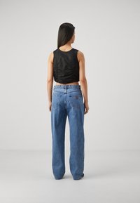 Top negro corto sin mangas con detalles fruncidos en la parte posterior, combinado con jeans de pierna ancha de cintura alta en azul claro que cuentan con bolsillos traseros.