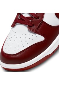 Red and white leather sneaker with perforated toe box, textured accents, and flat red laces. Design features a rounded shape and rubber sole.