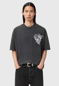 Īsām piedurkņu, tumši pelēka kokvilnas T-krekls ar grafikā attēlotu izkapti un lapām uz krūšu daļas. Brīvs piegriezums ar apļa veida kakla izgriezumu.