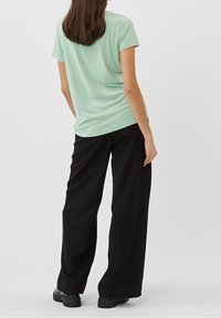 Kortærmet top i mintgrøn med løs pasform, kombineret med vidde sorte bukser og chunky sorte sko. Glat stof, minimalistisk design.