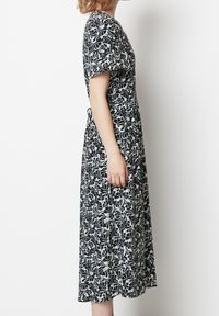 Svart och krämblommig klänning med korta ärmar, av avslappnad passform och med fickor, med en knälång design och mjuk tygkvalitet.