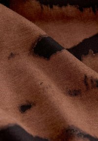Textile brun avec une texture douce, présentant un motif abstrait noir et de légères variations de couleur, créant une profondeur visuelle.