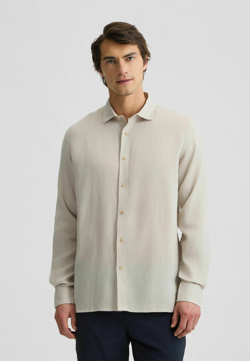 Camicia a maniche lunghe di un beige chiaro con colletto classico, caratterizzata da una sottile trama e sette bottoni sul davanti.