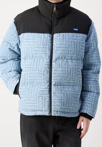 Kurtka ocieplana w kolorach jasnoniebieskim i czarnym z powtarzającym się wzorem logo „HUGO”, wysokim kołnierzem i zamkiem błyskawicznym.