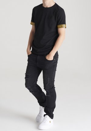 Zwarte t-shirt met gele gemêleerde accenten op de mouwen, gecombineerd met zwarte ripped jeans en witte sneakers. Casual pasvorm, eenvoudig ontwerp.