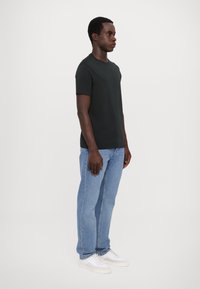 Černé tričko s krátkým rukávem, crew neck design, spárované s světle modrými džínami a bílými teniskami. Jednoduchý a klasický styl, jednobarevné.