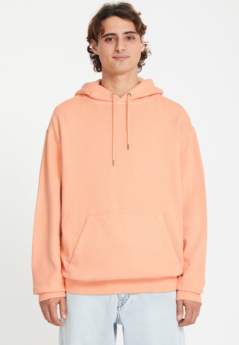 Hoodie de couleur pêche en tissu doux, avec une poche kangourou et une capuche à cordon. Poignets et ourlet côtelés, branding minimal.