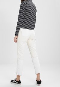 Czarna i biała bluzka w paski z długim rękawem, zestawiona z białymi dżinsami 7/8 z postrzępionymi brzegami, noszona z czarnymi trampkami.