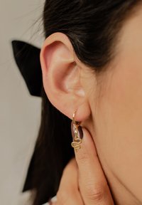 Pendiente de aro dorado con un diseño de serpiente, escalas texturizadas y un acabado pulido, llevado en la oreja de una persona con cabello oscuro.