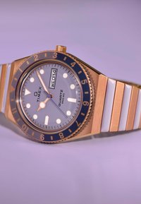 Orologio in quarzo color oro con quadrante grigio, ghiera blu, cinturino a righe bianche e oro, indici luminescenti e visualizzazione giorno/data alle 3.
