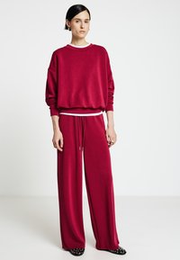 Felpa rossa in cotone con spalle scese e rifiniture bianche, abbinata a pantaloni ampi coordinati con vita con coulisse.