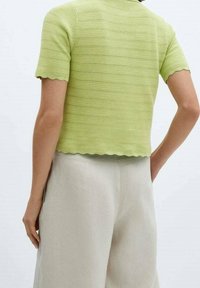 Limetkově zelený pletený crop top s krátkými rukávy a vlnitým lemem, doplněný béžovými lněnými kalhotami. Textura je žebrovaná a vrstvená.