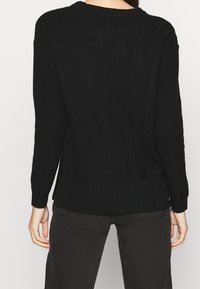 Pull noir en tricot avec texture côtelée, manches longues et coupe décontractée. Détail remarquable de maille torsadée à l'arrière.
