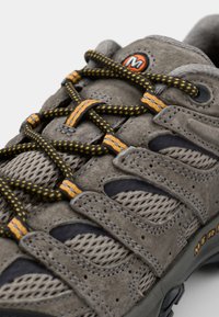 Grijze suede wandelschoen met meshpanelen, oranje en zwart patroon op de veters, versterkt teenstuk en een gestructureerde zool voor grip.