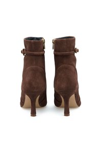 Stivaletti in suede marrone con tacco affusolato, chiusura con zip laterale e dettaglio a cinturino attorno alla caviglia. Texture liscia e silhouette aderente.
