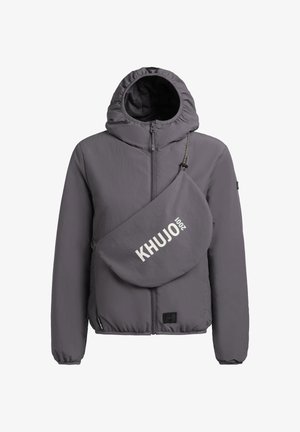 Harmaa hupullinen takki, jossa etuvetoketju ja sen kanssa yhteensopiva ristiin kannettava laukku, jossa rintakehässä teksti "KHUJO 2001".
