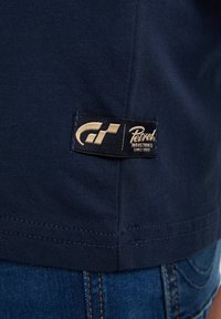 Námorně modré bavlněné tričko s viditelnými švy; zahrnuje černo-zlatou tkanou etiketu s nápisem "Petrol Industries."