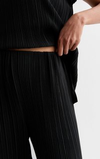 Svart plisserad topp och byxset i mjuk, texturerad tyg. Närbilden visar den elastiska midjan och detaljerad plissering.