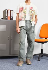 Koszula z krótkim rękawem w kwiatowy wzór, biała z czerwonymi i różowymi różami, zestawiona z zielonymi spodniami typu cargo. Noszona z beżowo-różowymi tenisówkami.