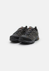 Schwarze und graue Sportschuhe aus strukturiertem Material, verstärkter Zeh, flexible Sohle und auffälliges Schnürsystem. Mit orangefarbenem Logoakzent.