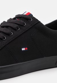 Baskets en toile noire à lacets, semelle en caoutchouc, avec un logo brodé comportant des accents rouges, blancs et bleus près de la languette.